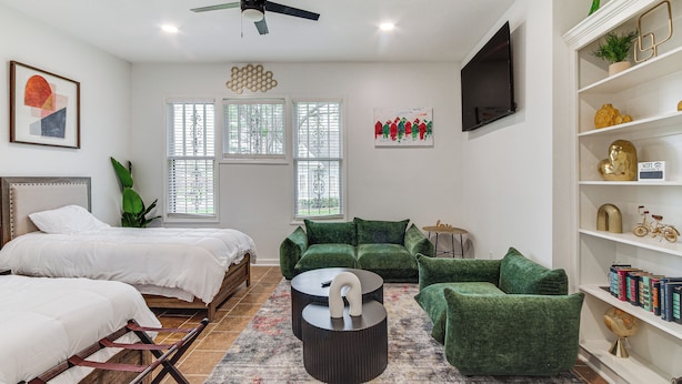 A modern bedroom with two beds, a green sofa set, a round coffee table, and a bookshelf. - Stylish Home ~ 2 Mi to Jackson State & Belhaven! (Jackson)