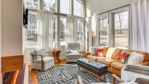 A spacious living room with large windows, a fireplace, a leather sofa, and a modern armchair. - Modern Lake House Retreat w/ Deck on Pickwick Lake (Counce)