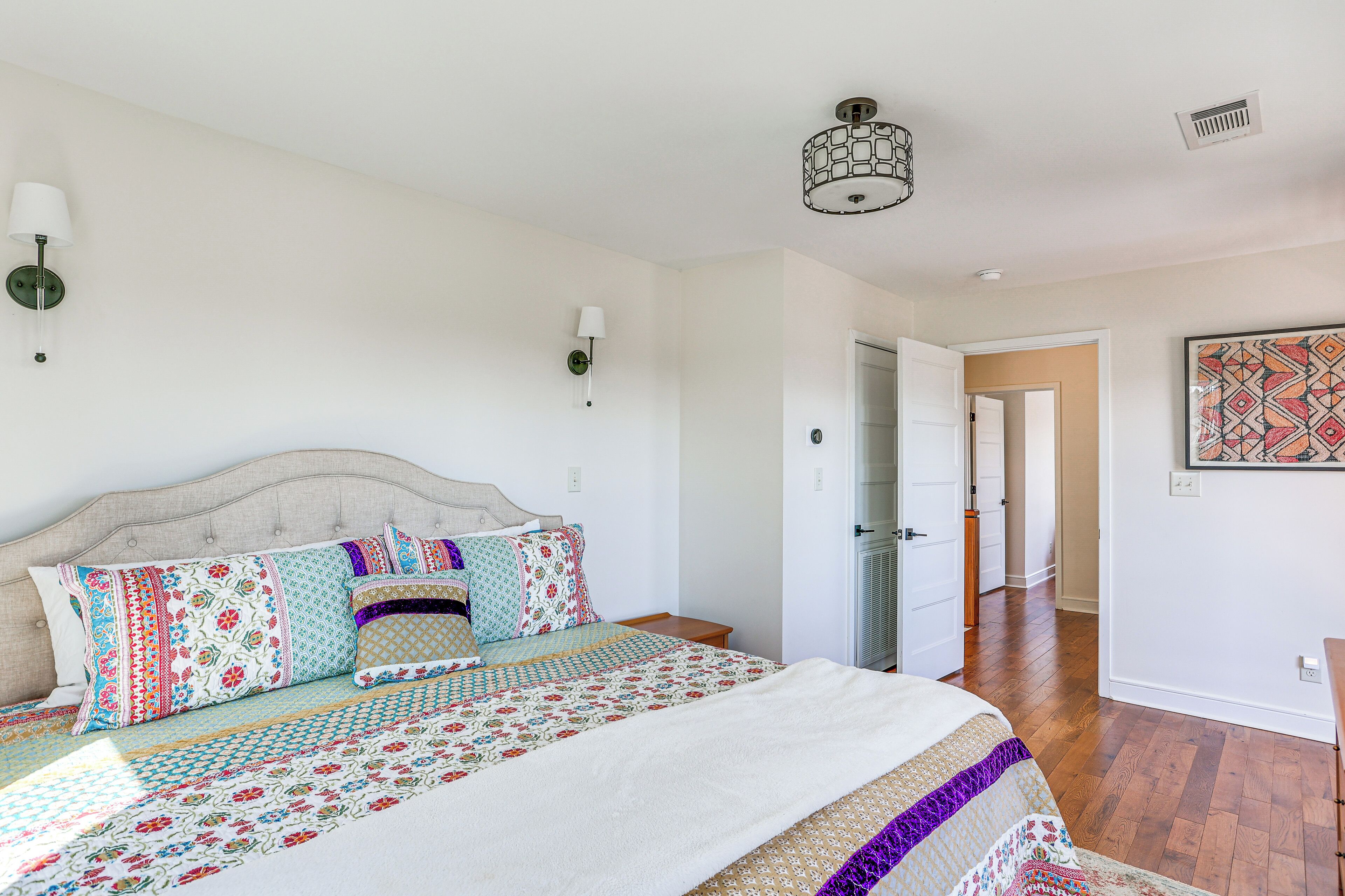 Een slaapkamer met een groot bed, een hoofdeinde, twee wandlampen en een deur naar een andere kamer.