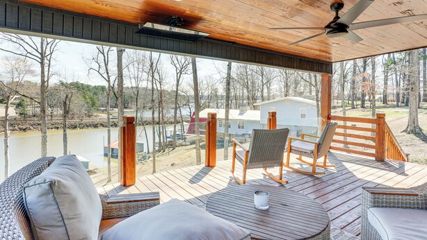 A wooden deck with outdoor furniture, a ceiling fan, and a view of a lake and buildings in the background. - Modern Lake House Retreat w/ Deck on Pickwick Lake (Counce)