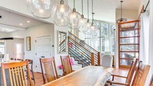 A spacious dining area with a large wooden table and chairs, a staircase with wooden railings, and large windows offering views of the outdoors. - Modern Lake House Retreat w/ Deck on Pickwick Lake (Counce)
