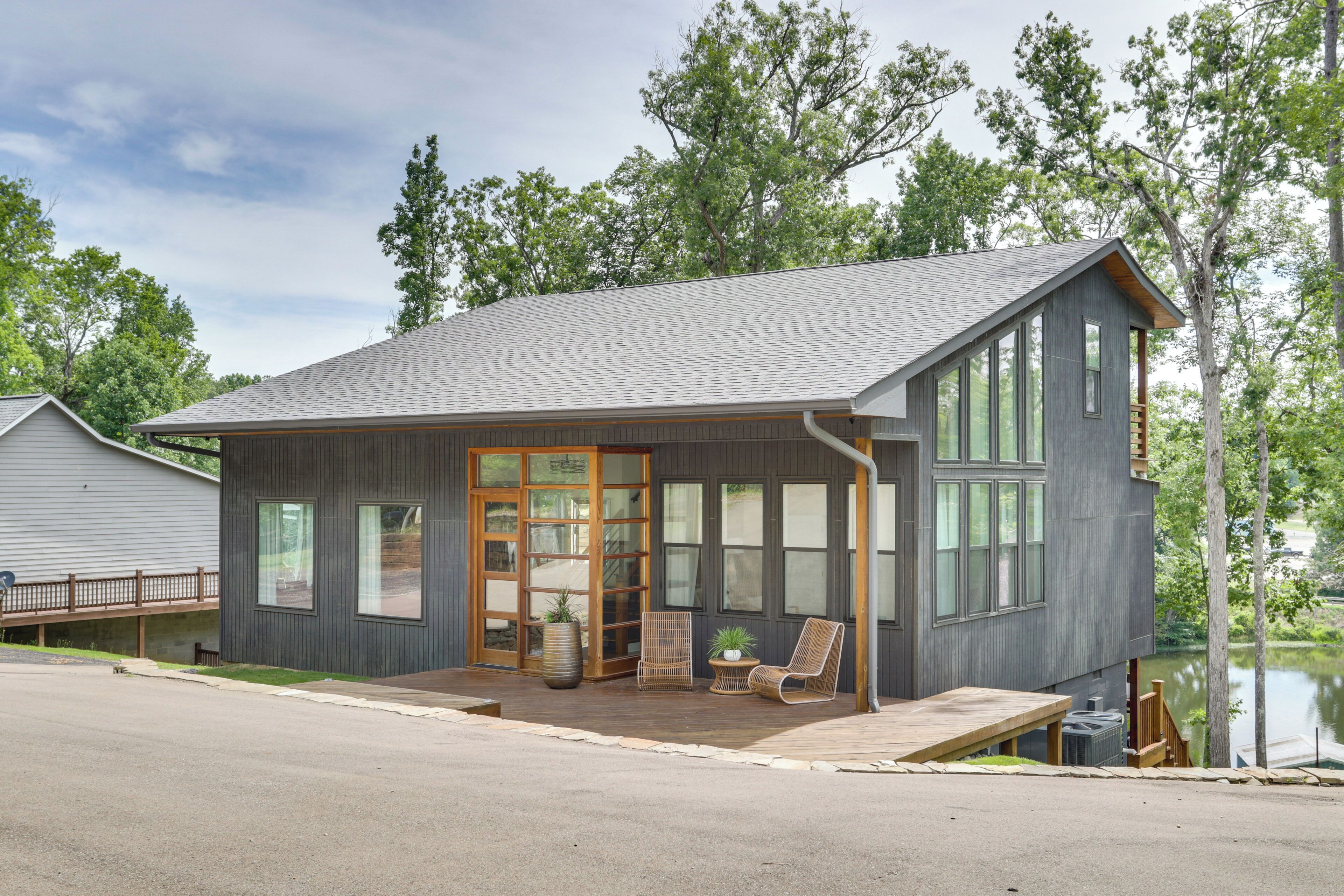 A modern two-story house with a covered porch, large windows, and a view of a lake.