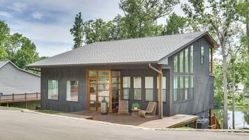 A modern two-story house with a covered porch, large windows, and a view of a lake.