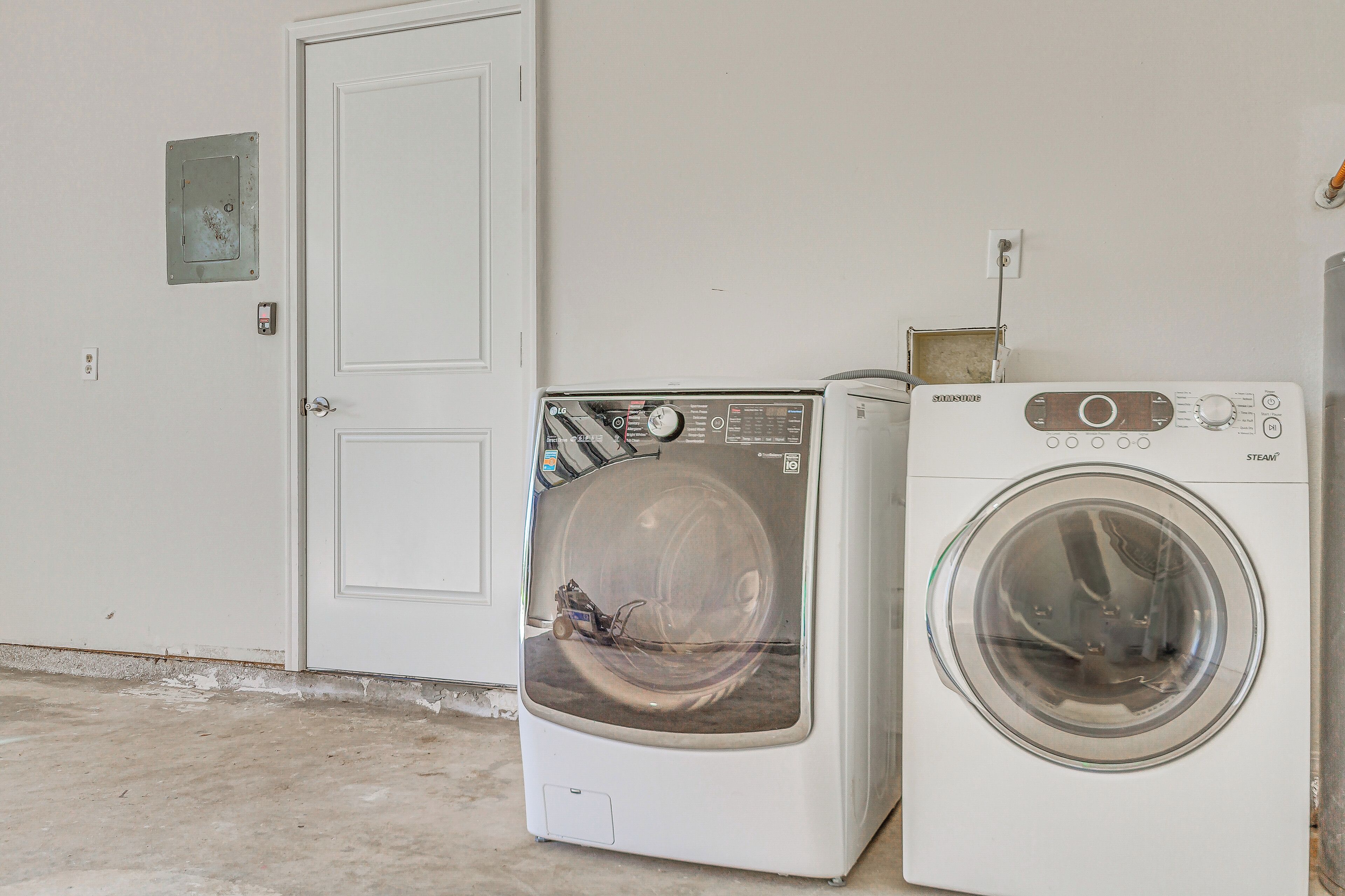 Two front-loading washing machines in a room with a white door and a concrete floor.