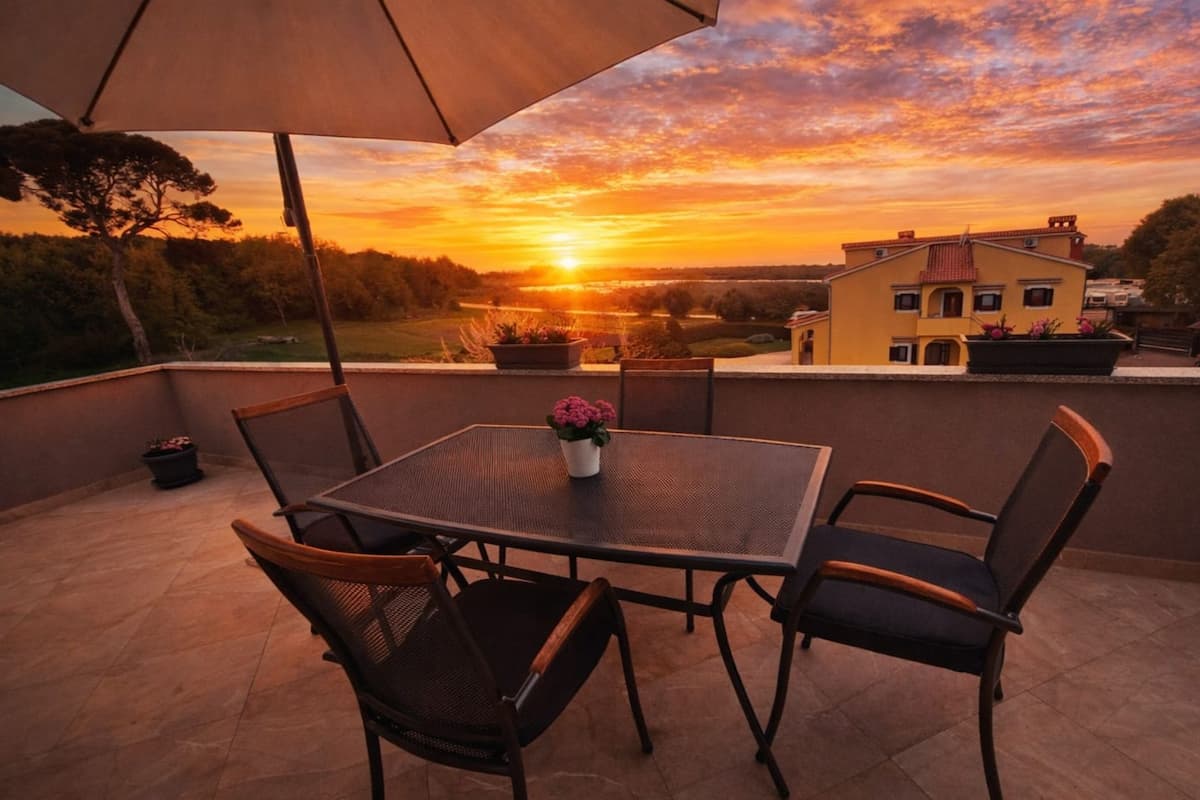 A patio with a table and chairs, an umbrella, and a sunset view.