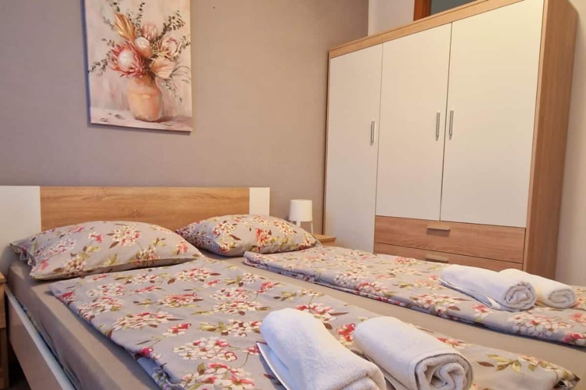 A double bed with floral bedding, a nightstand with a lamp, and a wardrobe with two doors.