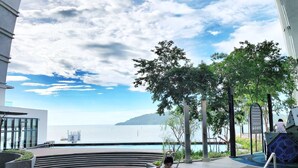 A modern hotel with a pool area, a child playing by the pool, and a view of the sea.
