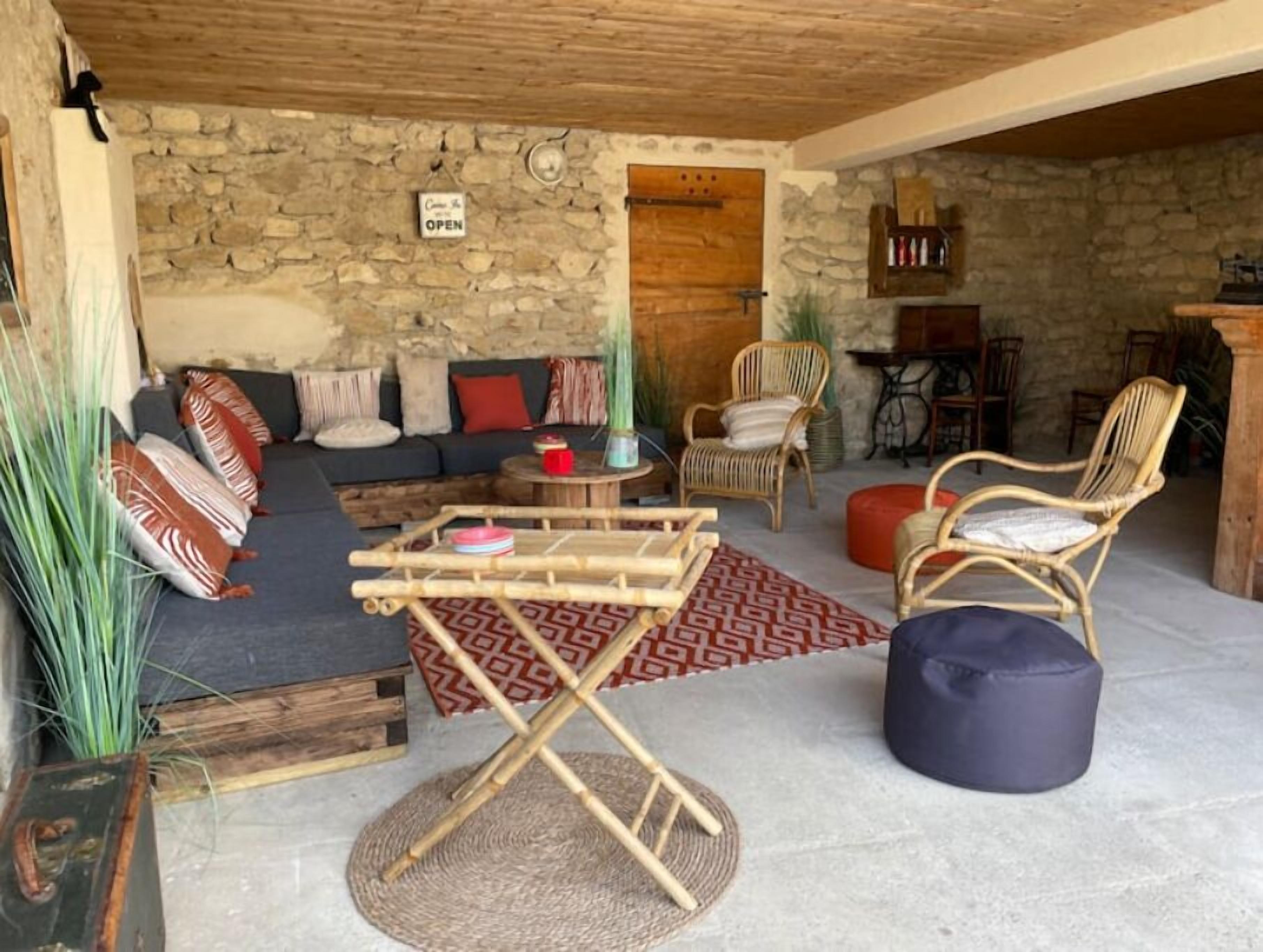 A cozy living area with a stone wall, a wooden ceiling, a sofa set, wicker chairs, and a coffee table.