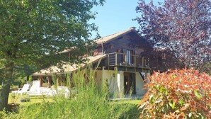 Une maison en bois à l’allure rustique, dotée d’un toit en pente, et entourée d’une végétation luxuriante et d’arbres.