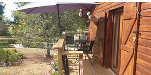A wooden deck with a table and chairs, a large umbrella, and a garden with potted plants and flowers.