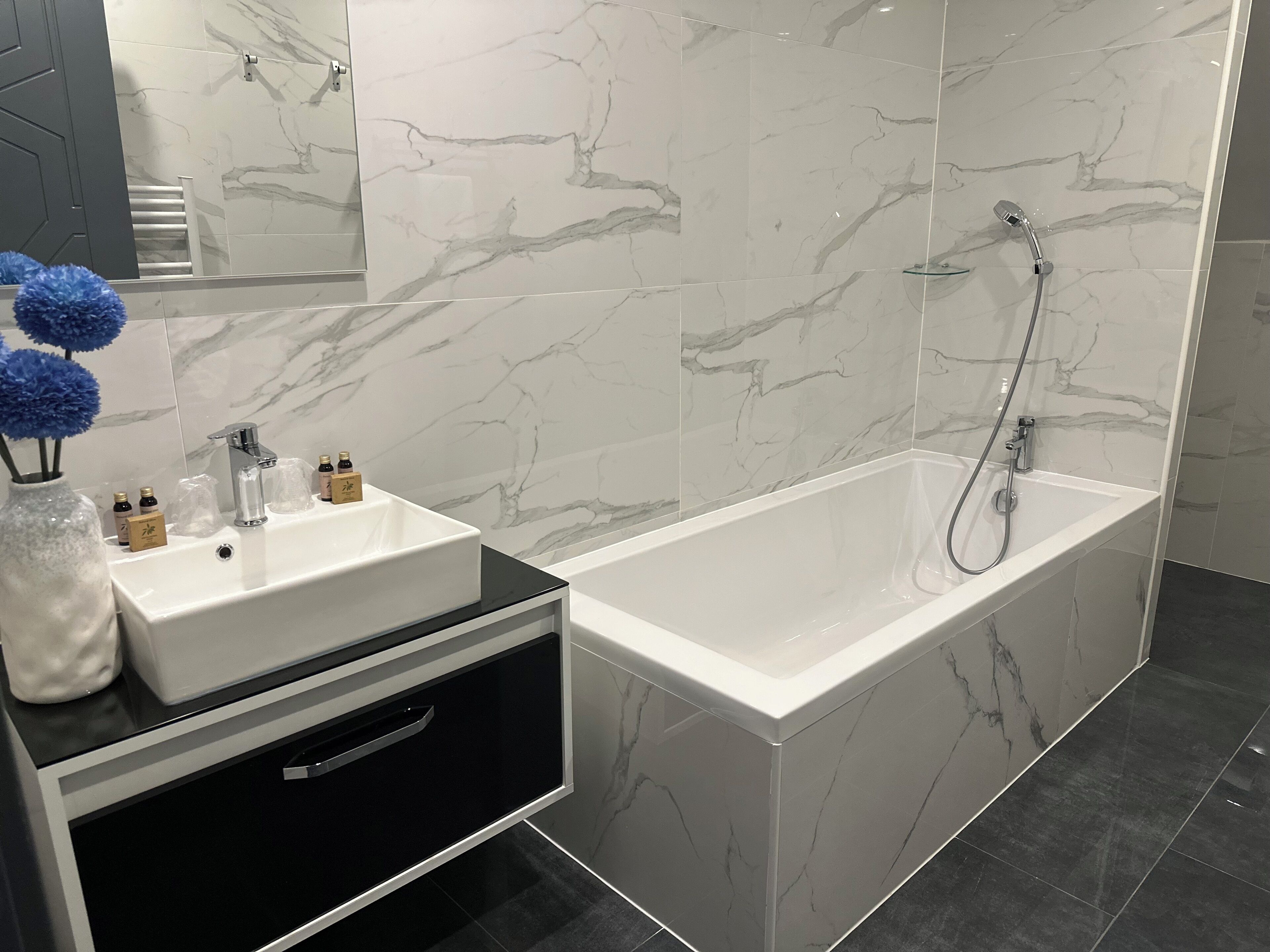 Un baño moderno con un lavabo de mármol blanco, un mueble de tocador negro y una zona de ducha independiente.