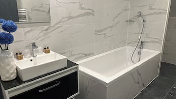 Un baño moderno con un lavabo de mármol blanco, un mueble de tocador negro y una zona de ducha independiente.