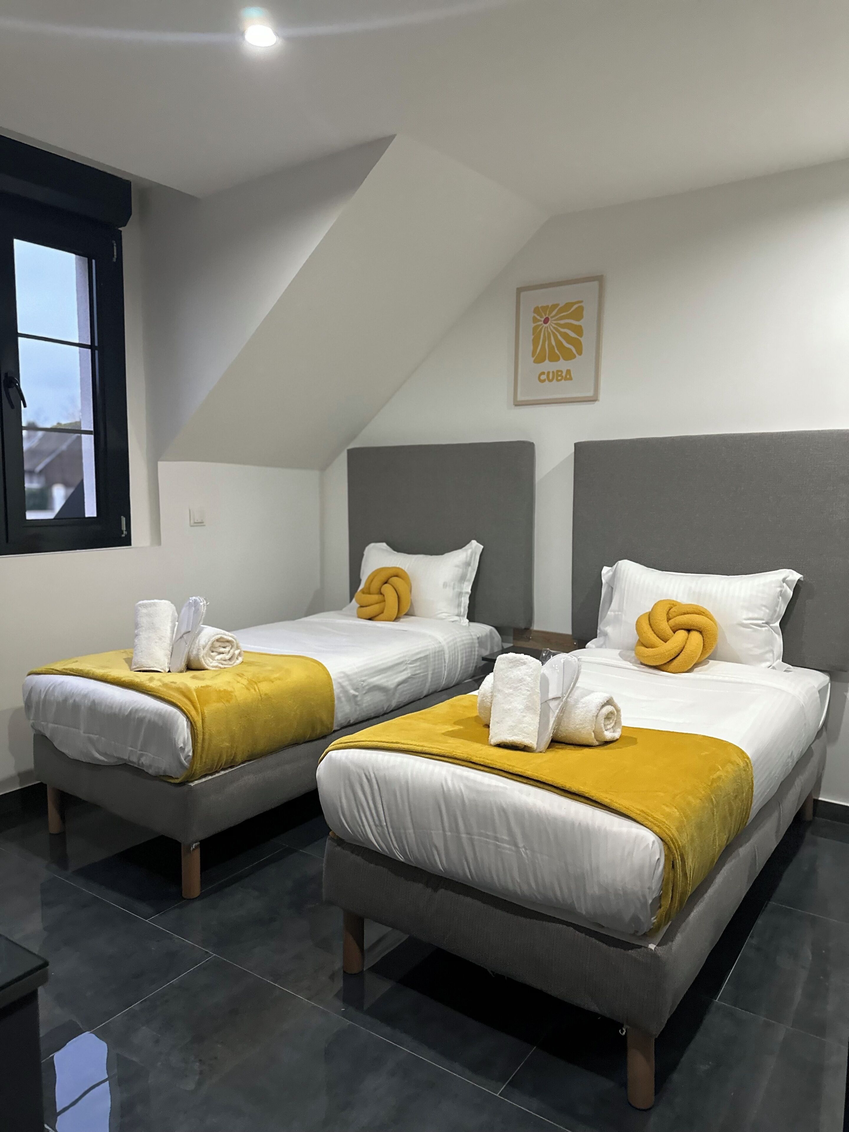 Een hotelkamer met twee eenpersoonsbedden, elk voorzien van een gele plaid en witte handdoeken.