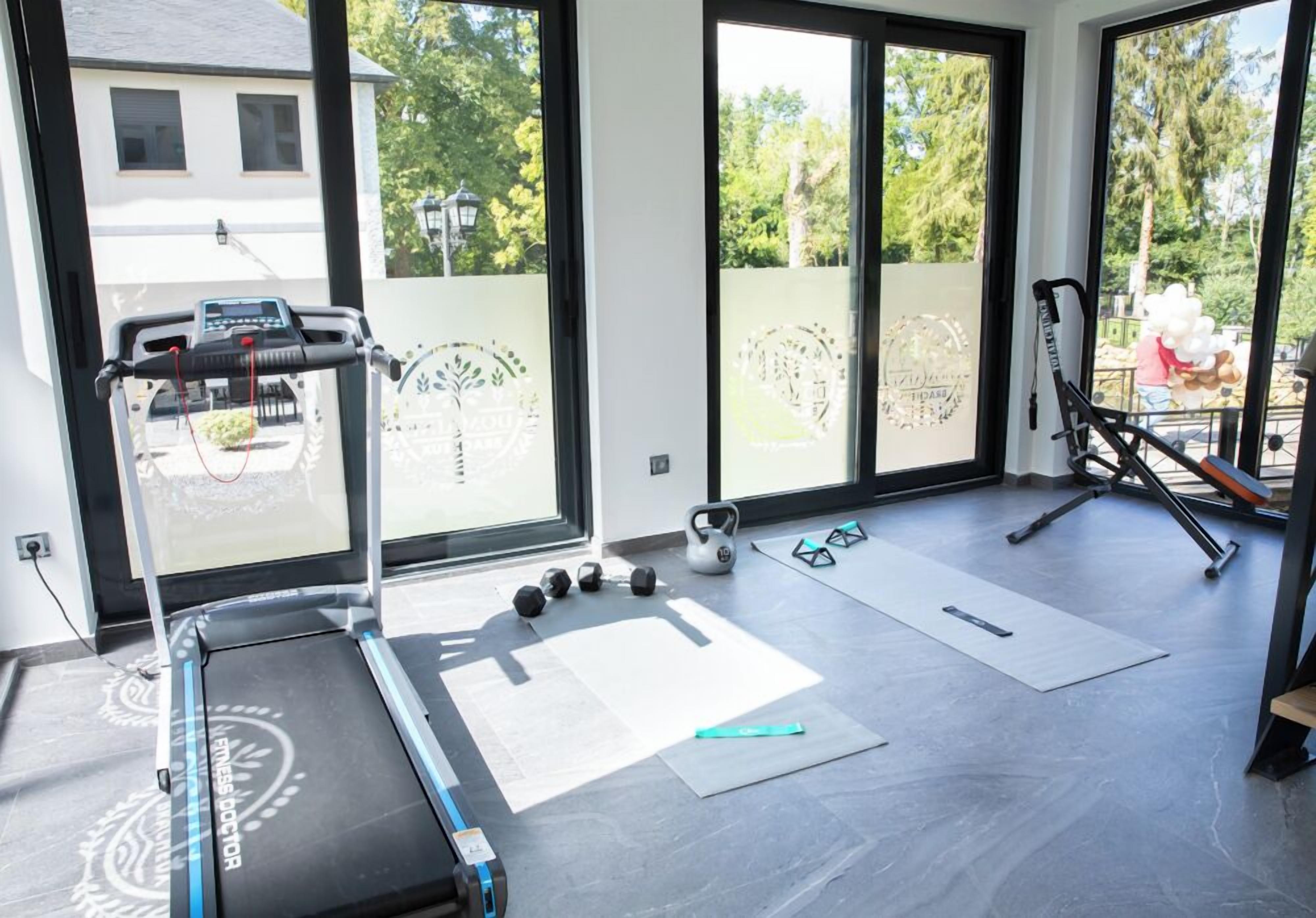 Un gimnasio en casa con una cinta de correr, mancuernas de kettlebell y colchonetas de ejercicio.