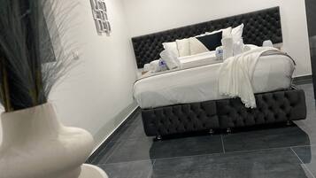 A modern bedroom with a tufted headboard, a neatly made bed with white linens, and a vase with dried plants on the left.