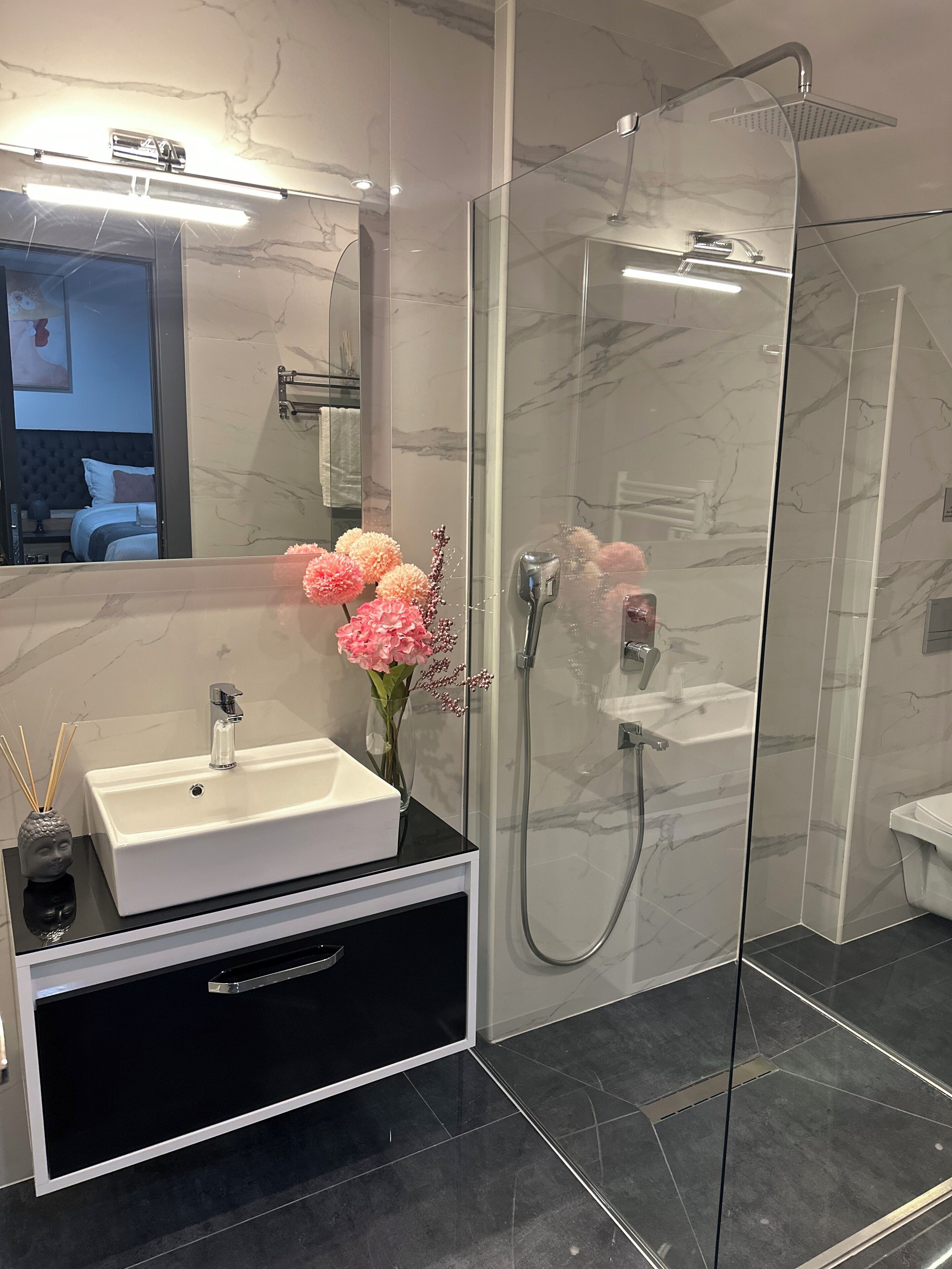 Un baño moderno con ducha de vidrio, lavamanos blanco y tocador negro.
