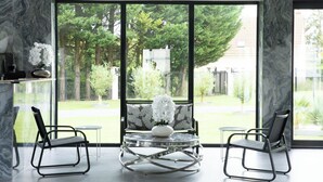 A modern room with large windows, a marble wall, and two black chairs around a glass table with a white vase. - Domaine de Bracheux (Fouquenies)