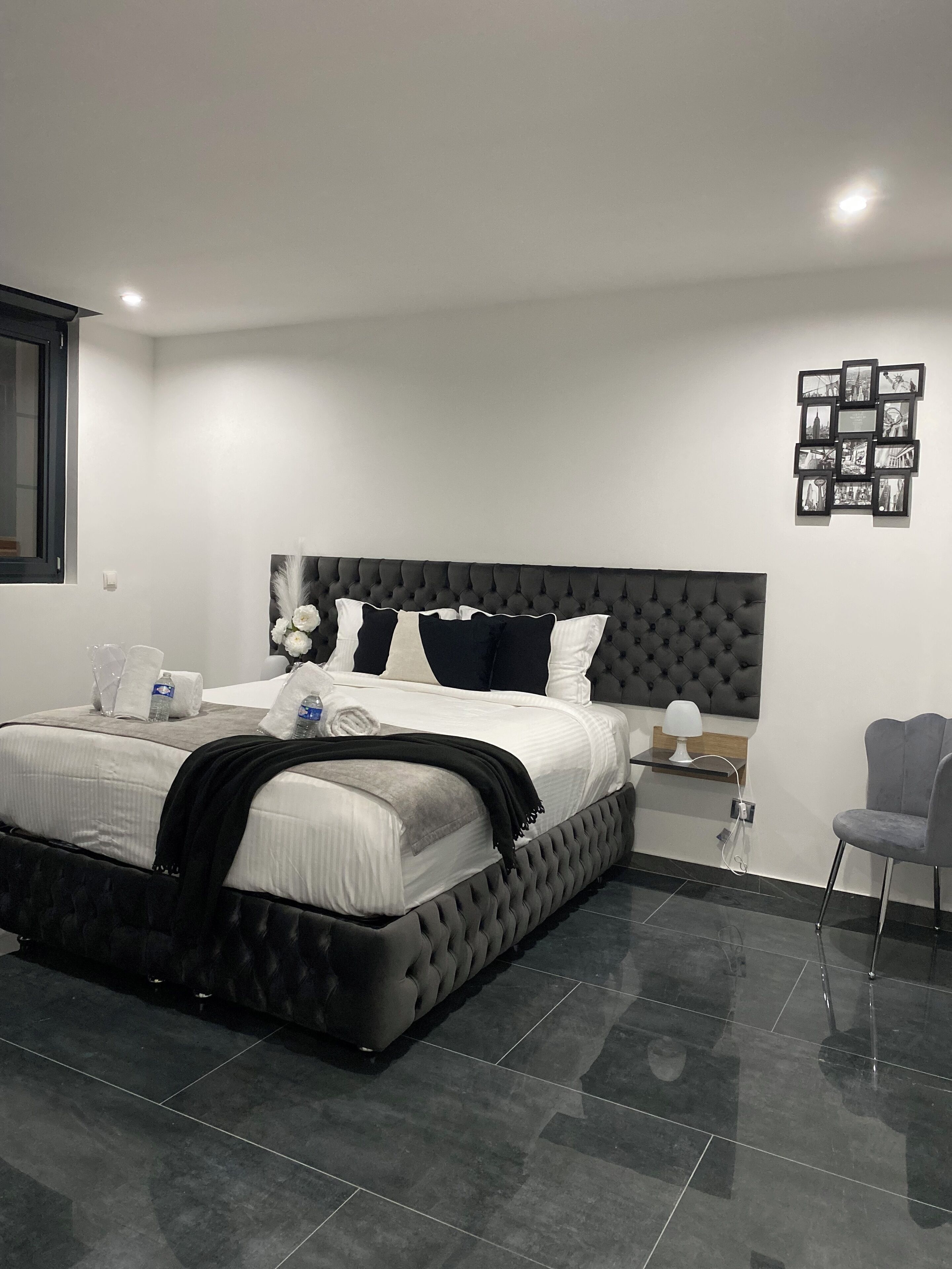 A modern bedroom with a tufted headboard, a neatly made bed, a bedside table with a lamp, and a chair.