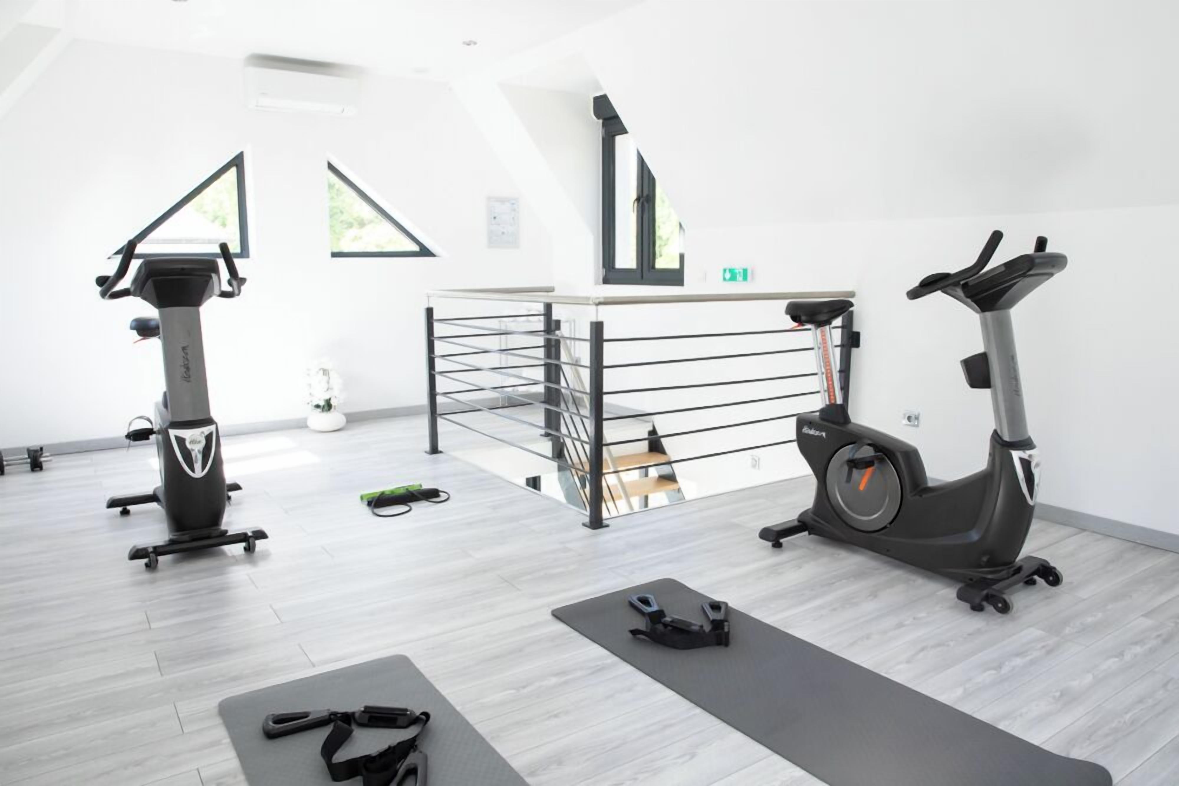 Un gimnasio moderno con dos bicicletas estáticas, una cinta de correr y colchonetas de ejercicio.