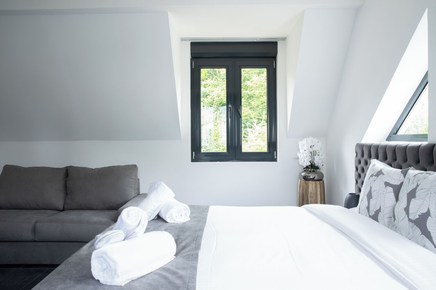 Ett modernt sovrum med en säng, en soffa och ett fönster med utsikt över grönområden.