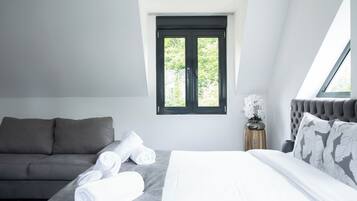 Ett modernt sovrum med en säng, en soffa och ett fönster med utsikt över grönområden.
