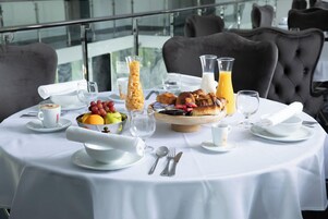 Una mesa redonda con una variedad de frutas, bollería y bebidas para el desayuno.