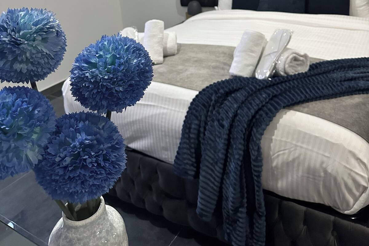 A modern bedroom with a tufted headboard, a large bed with white and grey bedding, a dark blue throw blanket, and a decorative wall piece above the bed.