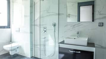 Ein modernes Badezimmer mit einer gläsernen Duschkabine, einem weißen Waschbecken und einer marmorverkleideten Wand.