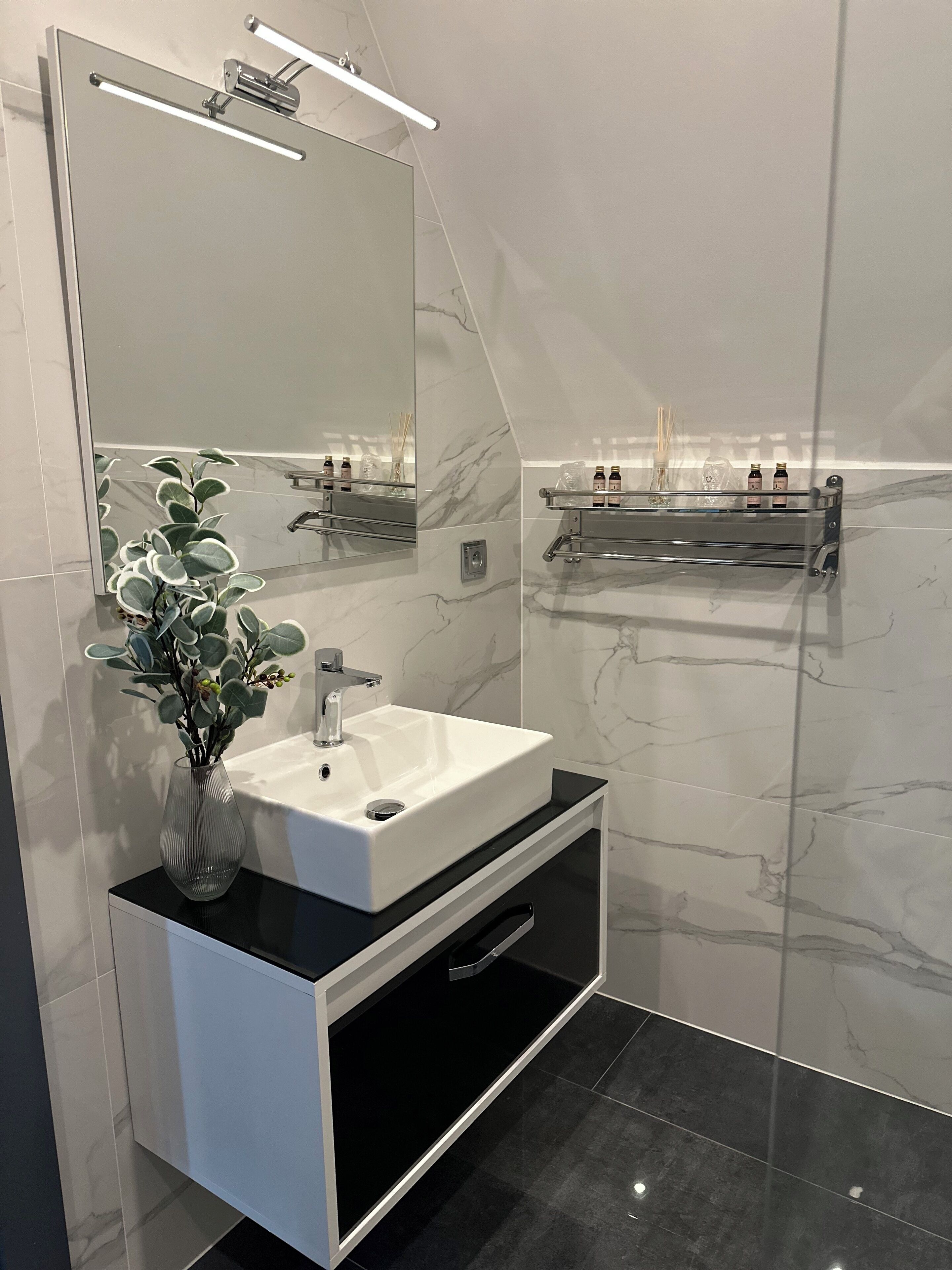 Un baño moderno con un lavamanos blanco, un espejo grande y una encimera negra.