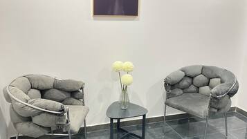 Ein Zimmer mit zwei grauen Sesseln, einem kleinen Tisch mit Blumenvase und einem gerahmten Kunstwerk an der Wand.