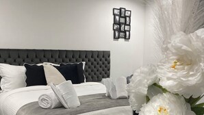 A modern bedroom with a tufted headboard, neatly made bed with white linens, and a decorative wall piece above the bed. - Domaine de Bracheux (Fouquenies)