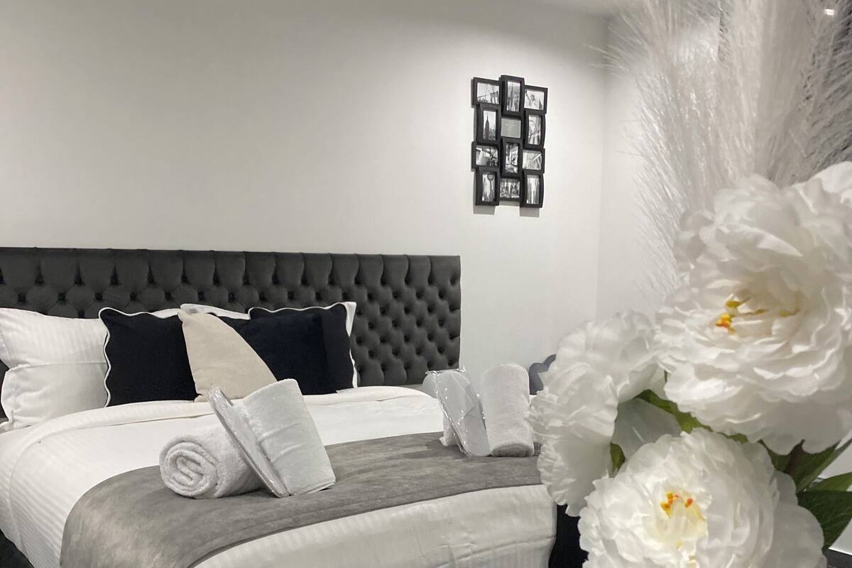 A modern bedroom with a tufted headboard, neatly made bed with white linens, and a decorative wall piece above the bed.