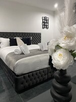 Un dormitorio moderno con cabecera capitonada, cama bien hecha con ropa blanca y un elemento decorativo sobre la cama.