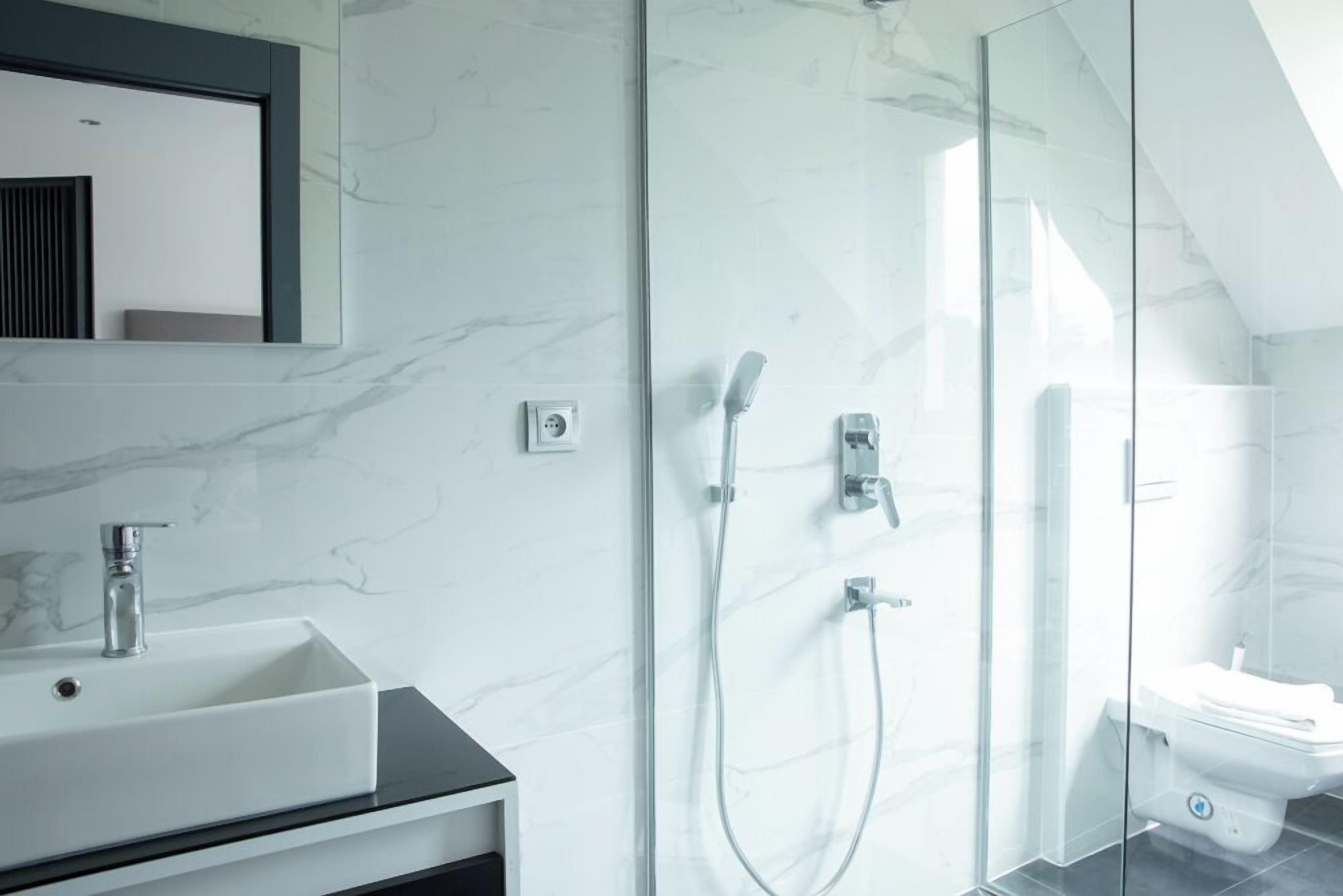 Un baño moderno con ducha envuelta en vidrio, un lavamanos blanco y un espejo sobre él.