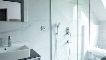 Un baño moderno con ducha envuelta en vidrio, un lavamanos blanco y un espejo sobre él.