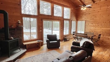 Un intérieur de chalet chaleureux avec une cheminée, un canapé en cuir, une table à manger et de grandes fenêtres.