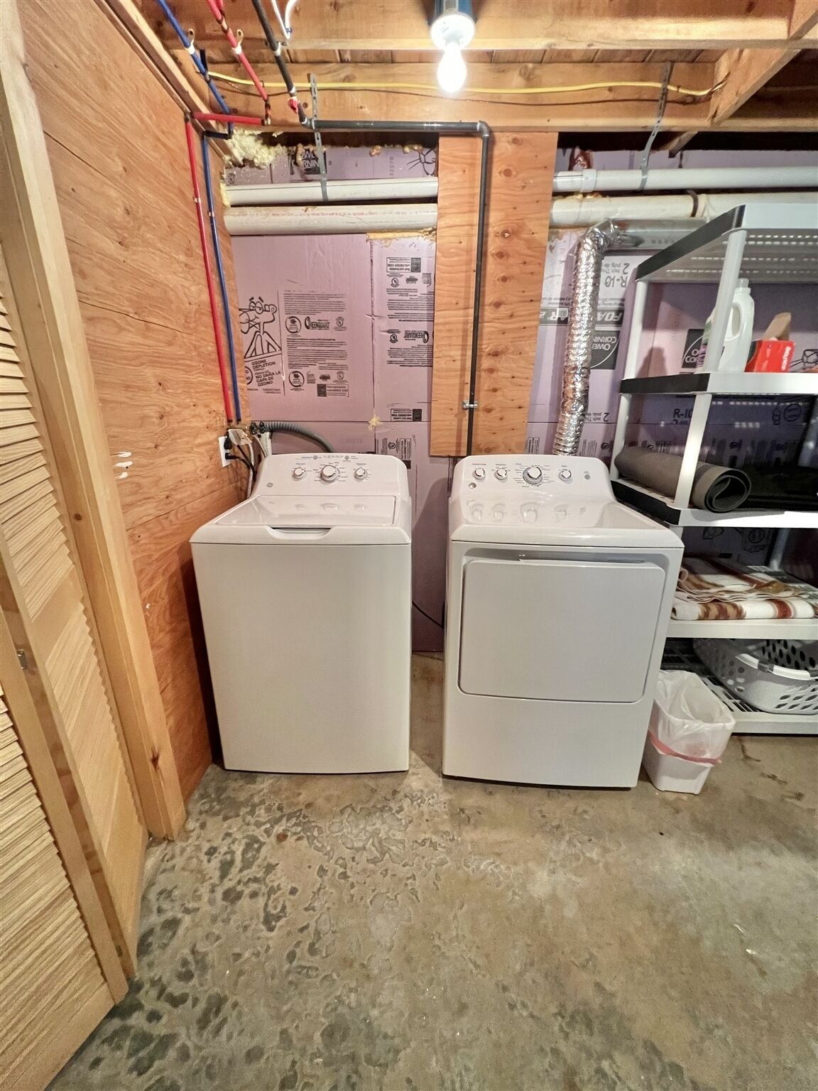 A laundry room with two white washing machines, wooden walls, and a concrete floor.