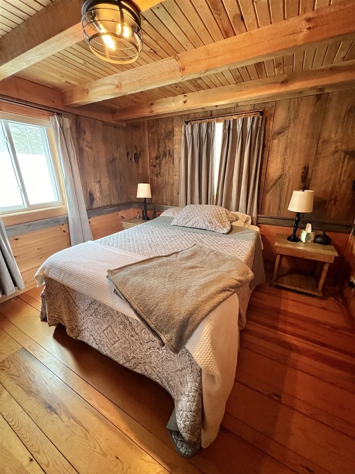 Une chambre aux murs lambrissés, avec deux lits, une fenêtre et un luminaire au plafond.