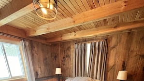 Dormitorio con paneles de madera, dos camas, una ventana y una lámpara en el techo.