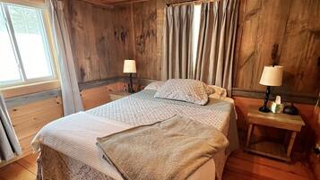 Une chambre aux murs lambrissés, avec deux lits, une fenêtre et un luminaire au plafond.