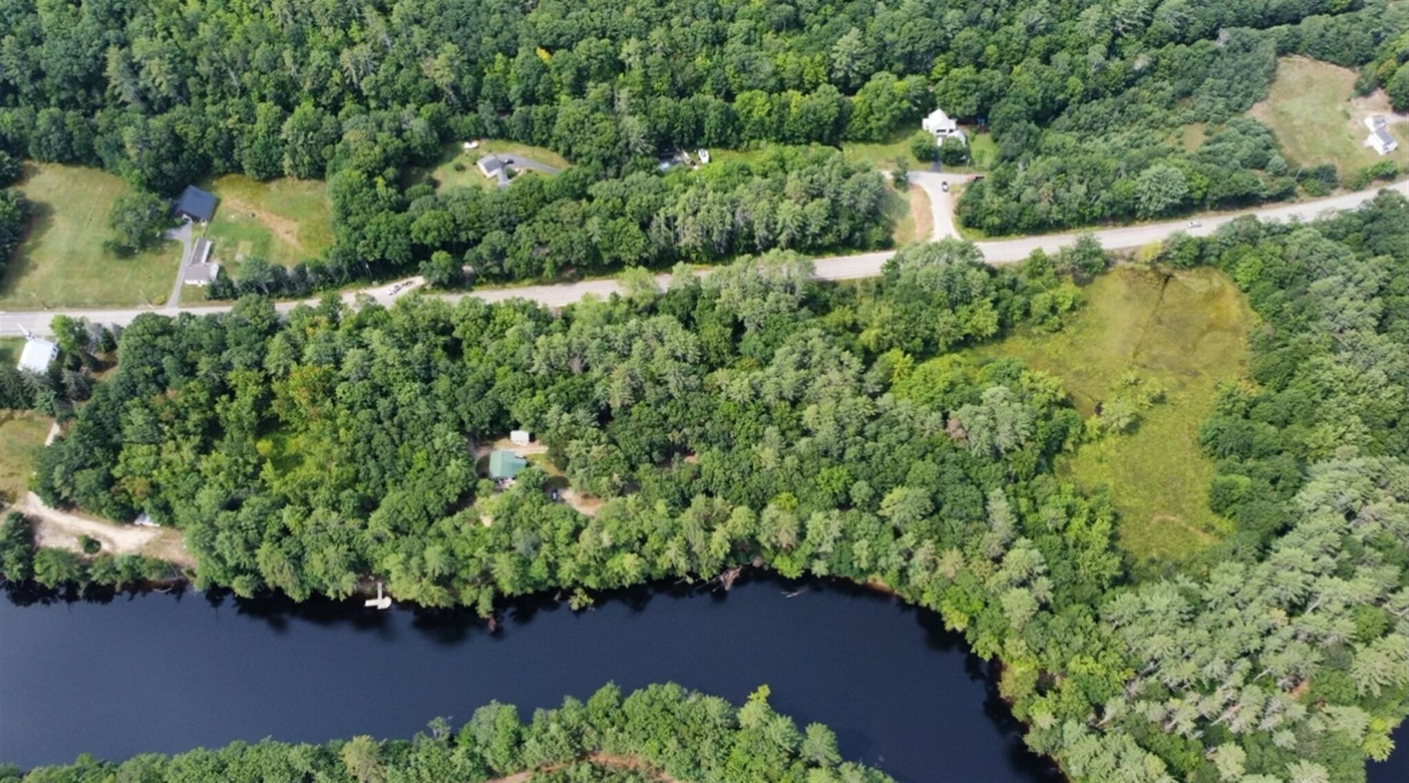 Luftaufnahme eines bewaldeten Gebiets mit einem See, Straßen und verstreuten Gebäuden.