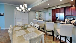 Une salle à manger agrémentée d’un lustre, une cuisine avec des meubles en bois foncé et un couloir avec une porte.