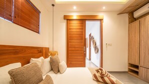 Un dormitorio moderno con cabecera de madera, una cama grande con muchos almohadones, una puerta de madera y un armario.
