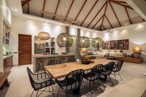 Une cuisine spacieuse avec une table à manger en bois, des chaises noires et des luminaires suspendus.
