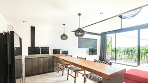 A modern kitchen with a long wooden table, bar stools, and pendant lighting.