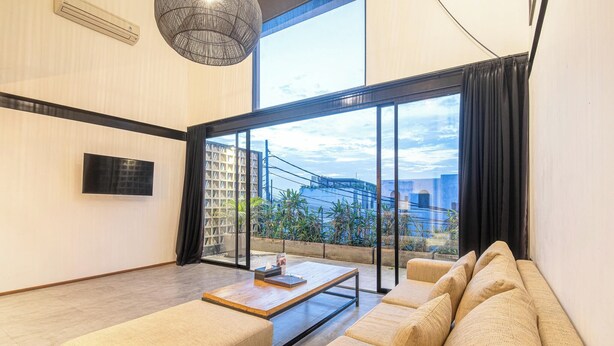 A spacious living room with a large window, a flat-screen TV, and a comfortable sofa. - Expansive Loft 200m from Canggu Beach Haven<br>Part of Noma Estate (Pererenan)