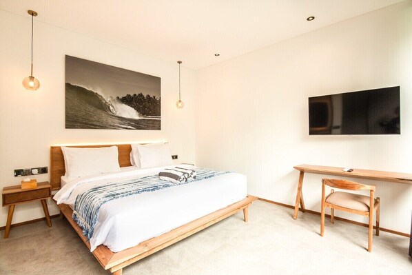 Un dormitorio con cama, mesita de noche, escritorio, silla y un televisor grande montado en la pared.