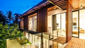 Una casa moderna con balcón de cristal, terraza de madera y un interior bien iluminado.