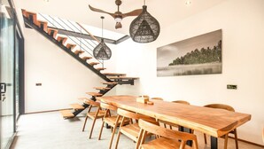 Un interior moderno con una mesa de comedor de madera, sillas y una escalera con barandilla de vidrio.