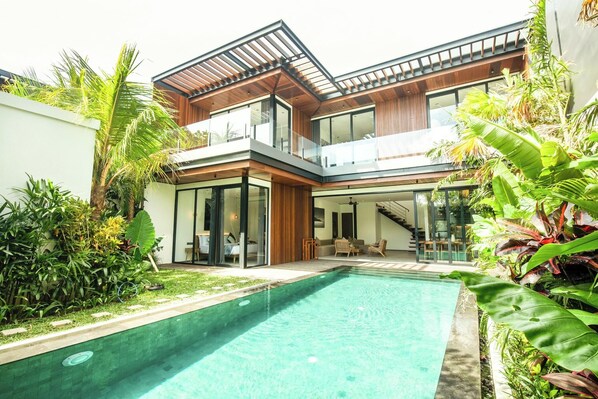Ein modernes, zweistöckiges Haus mit Swimmingpool, großen Glasfenstern und einem Balkon.